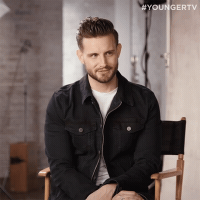A Man In A Black Jacket Sits In A Director 'S Chair With #Youngertv Written Above Him GIF