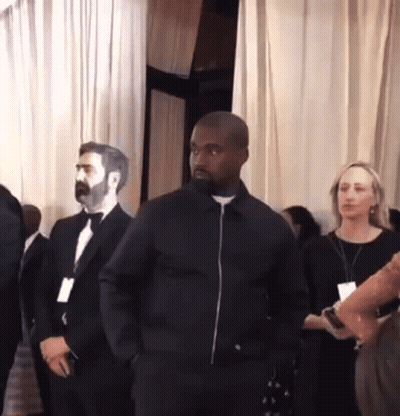 A Man In A Black Jacket Stands In A Room With Other People GIF