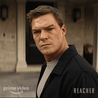 A Man In A Black Jacket Stands In Front Of A Building With Reacher Written On It GIF