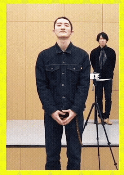 A Man In A Black Jacket Stands In Front Of A Camera GIF