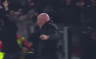 A Man In A Black Jacket Stands In Front Of A Crowd Wearing A Yellow Vest That Says ' Emergency ' On It GIF