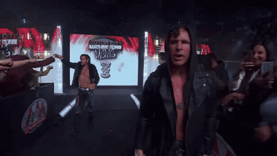 A Man In A Black Jacket Stands In Front Of A Screen That Says Authority Machine Gun GIF