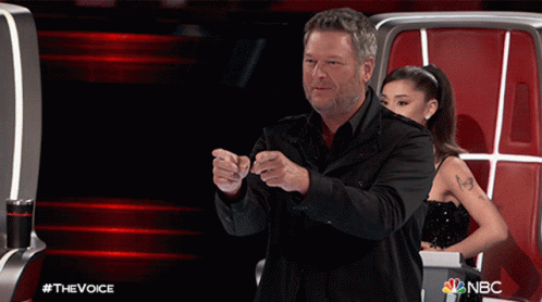 A Man In A Black Jacket Stands In Front Of A Woman In A Black Dress On A Nbc Show Called The Voice GIF