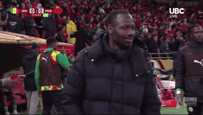 A Man In A Black Jacket Stands On A Soccer Field In Front Of A Crowd With Ubc Live Written On The Bottom GIF