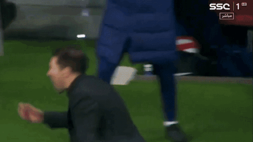 A Man In A Black Jacket Stands On A Soccer Field With Ssc In The Corner GIF