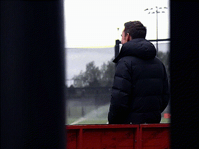 A Man In A Black Jacket With A Hood Looks Out A Window GIF