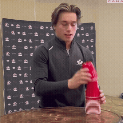A Man In A Black Jacket With A Maple Leaf On It Stacks Red Cups GIF
