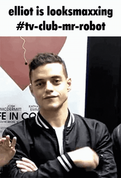A Man In A Black Jacket With His Arms Crossed Is Standing In Front Of A Red Heart . GIF