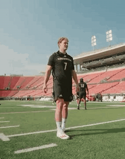 A Man In A Black Jersey Is Standing On A Football Field . GIF
