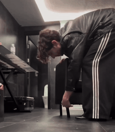 A Man In A Black Leather Jacket And White Stripped Pants Is Bending Over GIF