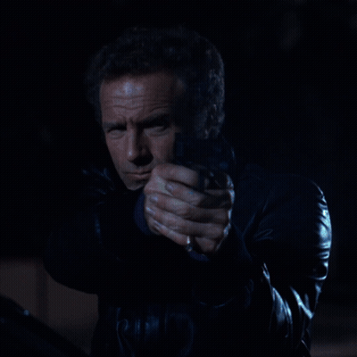A Man In A Black Leather Jacket Is Holding A Gun In His Hand GIF
