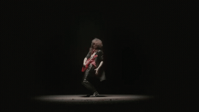 A Man In A Black Leather Jacket Is Playing A Red Electric Guitar In The Dark . GIF