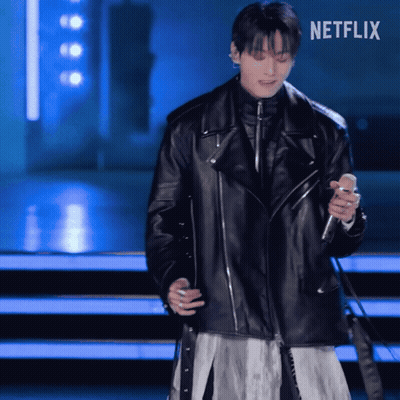 A Man In A Black Leather Jacket Is Singing Into A Microphone With Netflix Written On The Bottom GIF