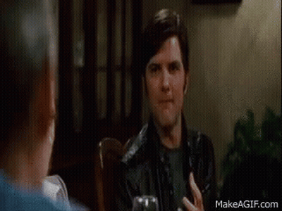 A Man In A Black Leather Jacket Is Sitting At A Table With A Glass Of Wine . GIF