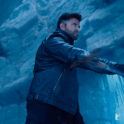 A Man In A Black Leather Jacket Is Standing In Front Of A Blue Wall GIF