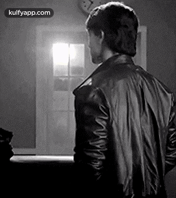 A Man In A Black Leather Jacket Is Standing In Front Of A Window . GIF