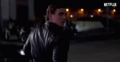 A Man In A Black Leather Jacket Is Standing On A Street At Night . GIF