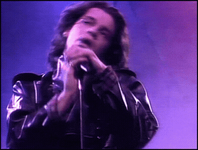 A Man In A Black Leather Jacket Singing Into A Microphone GIF