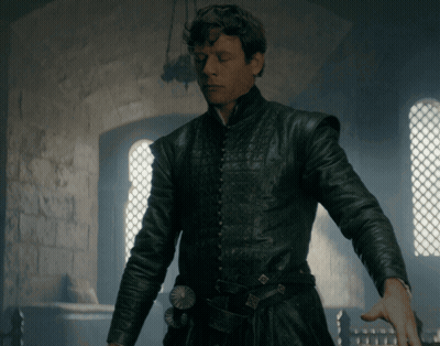A Man In A Black Leather Jacket Stands In Front Of A Brick Wall GIF