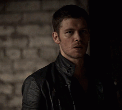 A Man In A Black Leather Jacket Stands In The Dark GIF