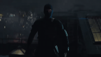 A Man In A Black Mask Is Standing In The Dark Holding A Gun . GIF