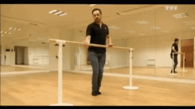 A Man In A Black Polo Shirt Is Holding A Bar In A Dance Studio . GIF