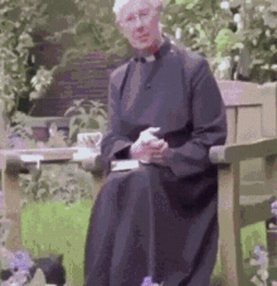 A Man In A Black Robe Is Sitting On A Bench In A Garden GIF