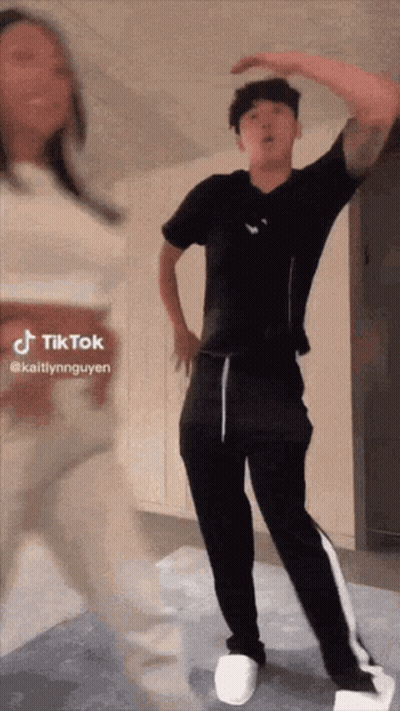 A Man In A Black Shirt And Black Pants Is Dancing With A Woman In A White Dress . GIF