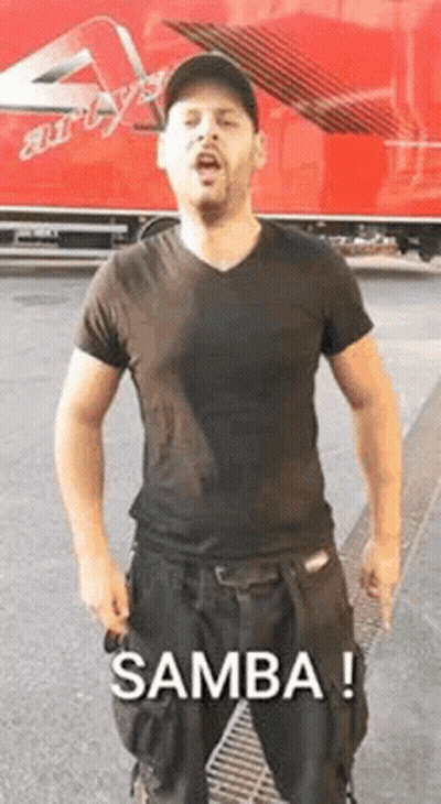 A Man In A Black Shirt And Black Pants Is Standing In Front Of A Red Truck And Singing . GIF
