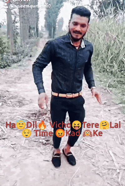 A Man In A Black Shirt And Black Pants Is Standing On A Dirt Path GIF
