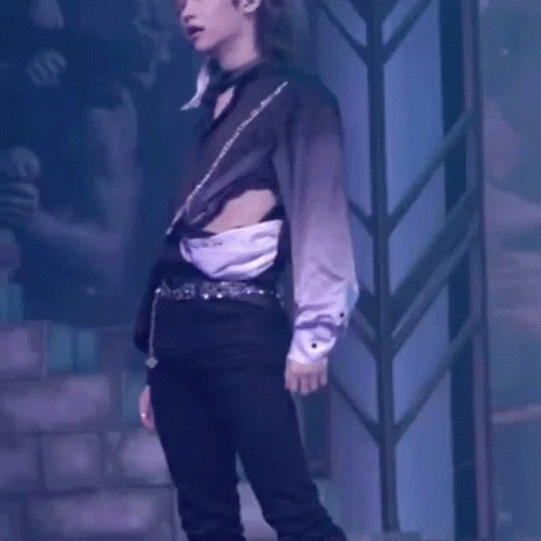 A Man In A Black Shirt And Black Pants Is Standing On A Stage With His Shirt Cut Off . GIF