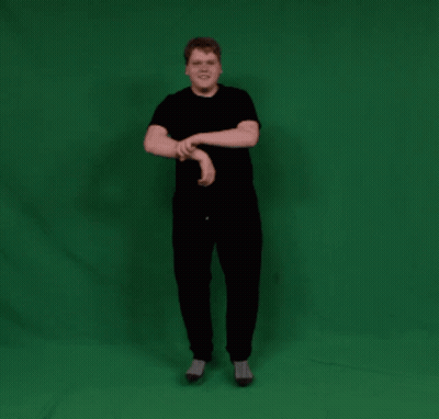 A Man In A Black Shirt And Black Pants Stands In Front Of A Green Screen GIF