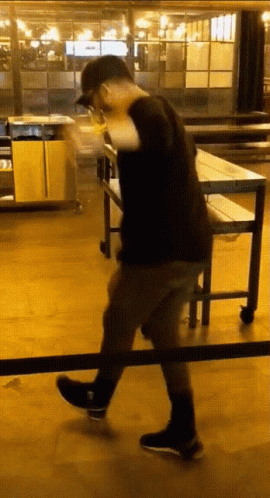 A Man In A Black Shirt And Black Shoes Is Walking Across A Wooden Floor GIF