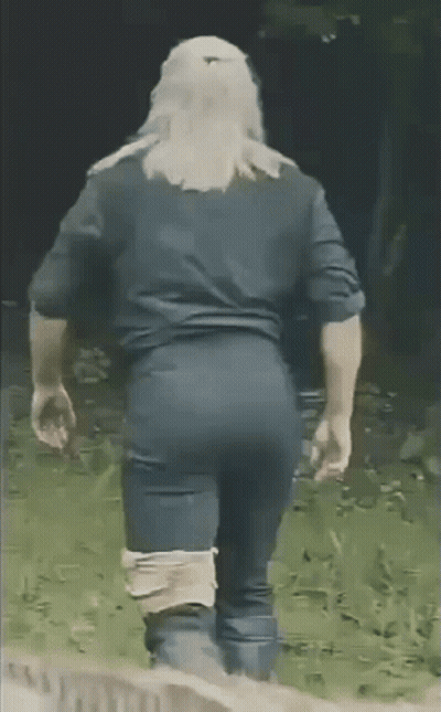 A Man In A Black Shirt And Blue Pants Is Walking In The Grass . GIF