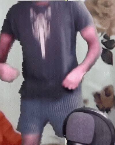 A Man In A Black Shirt And Blue Shorts Is Standing In Front Of A Microphone . GIF