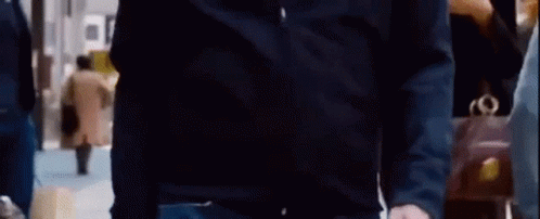 A Man In A Black Shirt And Jeans Is Standing In A Crowded Room . GIF