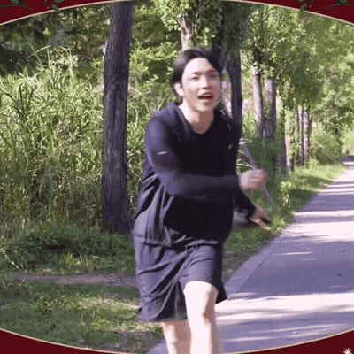 A Man In A Black Shirt And Shorts Is Running Down A Path In The Woods GIF