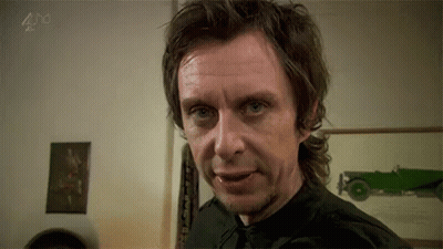 A Man In A Black Shirt And Tie Is Making A Funny Face In A Room . GIF