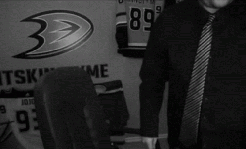 A Man In A Black Shirt And Tie Is Standing In Front Of A Wall That Says " Wasted " GIF