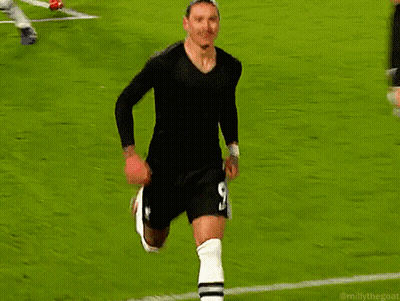 A Man In A Black Shirt And White Socks Stands On A Soccer Field Next To A Red Flag GIF
