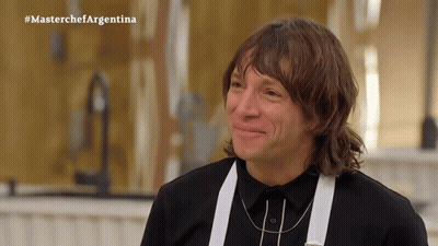 A Man In A Black Shirt And White Suspenders Is Smiling In Front Of A Masterchef Argentina Sign GIF