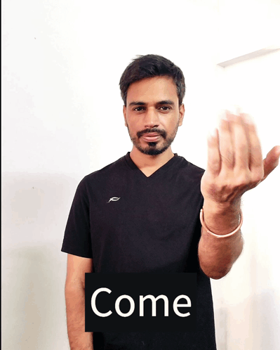 A Man In A Black Shirt Holds Up His Hand In Front Of A Sign That Reads Come GIF