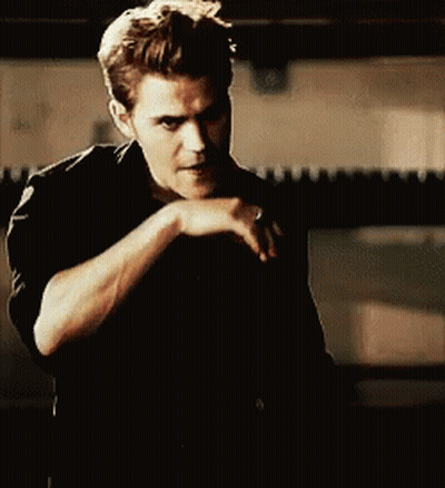 A Man In A Black Shirt Is Covering His Mouth With His Hand While Looking At The Camera . GIF