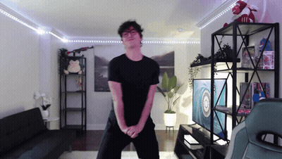 A Man In A Black Shirt Is Dancing In A Living Room With A Target On The Wall GIF