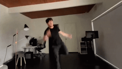 A Man In A Black Shirt Is Dancing In A Room With A Desk And Chair GIF