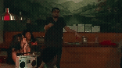 A Man In A Black Shirt Is Dancing In A Room With A Group Of People . GIF