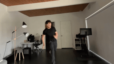 A Man In A Black Shirt Is Dancing In A Room With A Monitor On A Stand GIF