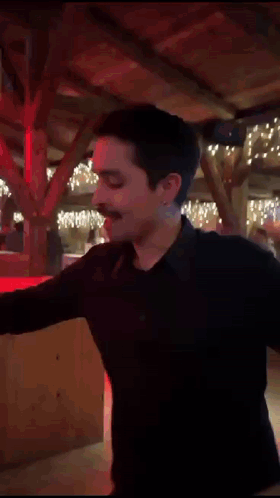 A Man In A Black Shirt Is Dancing In A Room With Christmas Lights On The Ceiling . GIF