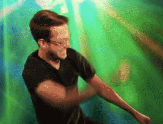 A Man In A Black Shirt Is Dancing In Front Of A Green Backdrop GIF