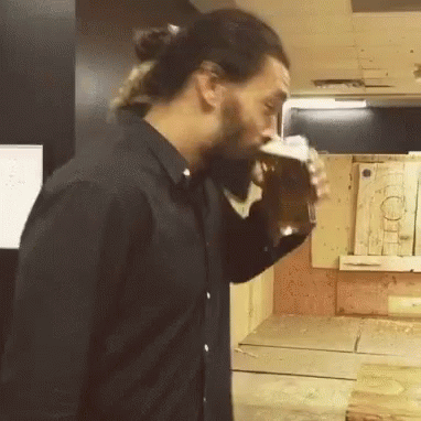 A Man In A Black Shirt Is Drinking A Beer From A Glass GIF